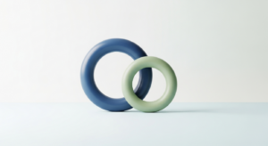 Two interlocking torus shapes in blue and pale green resting on a pale surface, symbolizing connection and unity.